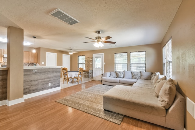 living room with a textured ceiling, ceiling fan, and light hardwood / wood-style floors