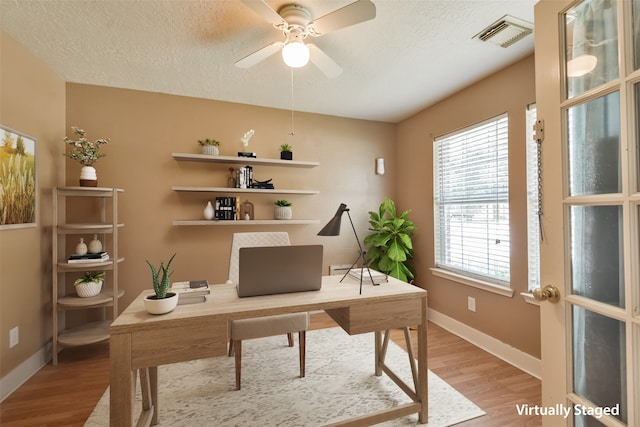 office space with ceiling fan, light wood-type flooring, a textured ceiling, and a wealth of natural light