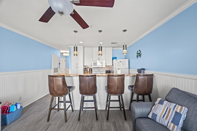 kitchen featuring white cabinets, dark hardwood / wood-style flooring, a kitchen bar, hanging light fixtures, and white appliances