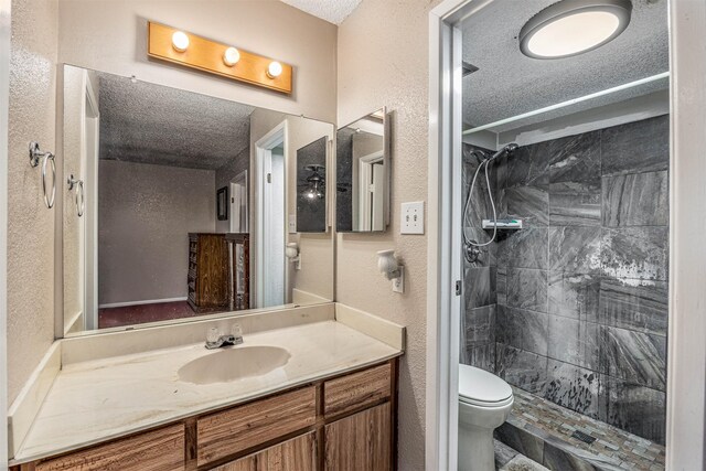 bathroom with vanity, a tile shower, toilet, a textured ceiling, and tile patterned flooring