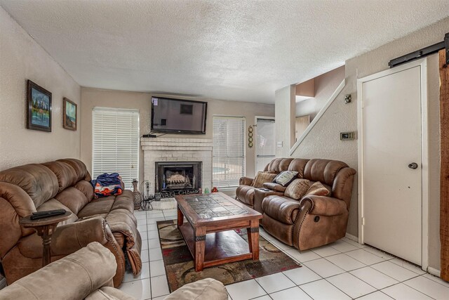 living room featuring a textured ceiling, a barn door, a fireplace, and light tile patterned floors