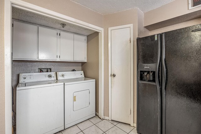 clothes washing area with washing machine and dryer, a textured ceiling, cabinets, and light tile patterned floors