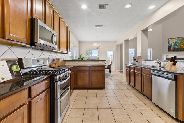 kitchen featuring dark stone countertops, sink, an inviting chandelier, hanging light fixtures, and stainless steel appliances