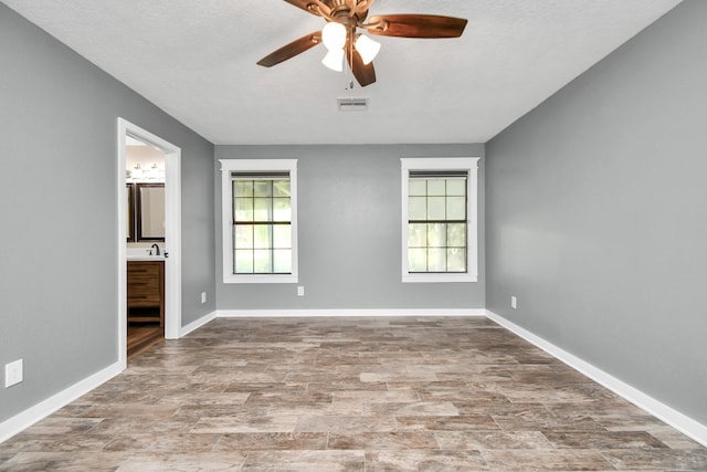 unfurnished bedroom featuring multiple windows, ensuite bathroom, ceiling fan, and a textured ceiling