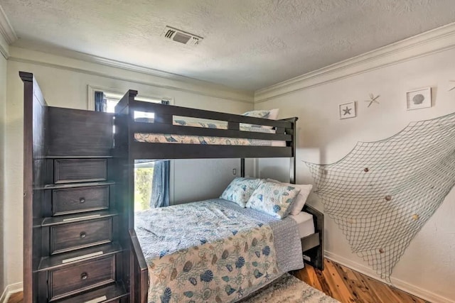 bedroom featuring a textured ceiling, wood finished floors, visible vents, baseboards, and ornamental molding