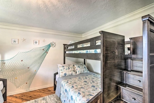 bedroom with a textured ceiling, baseboards, wood finished floors, and crown molding