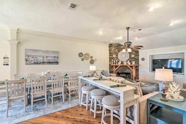 dining space featuring visible vents, a ceiling fan, a wainscoted wall, wood finished floors, and a stone fireplace