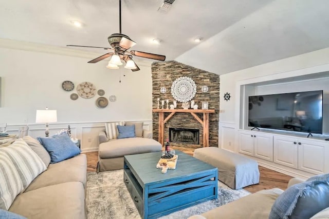 living area with light wood finished floors, lofted ceiling, visible vents, wainscoting, and a stone fireplace