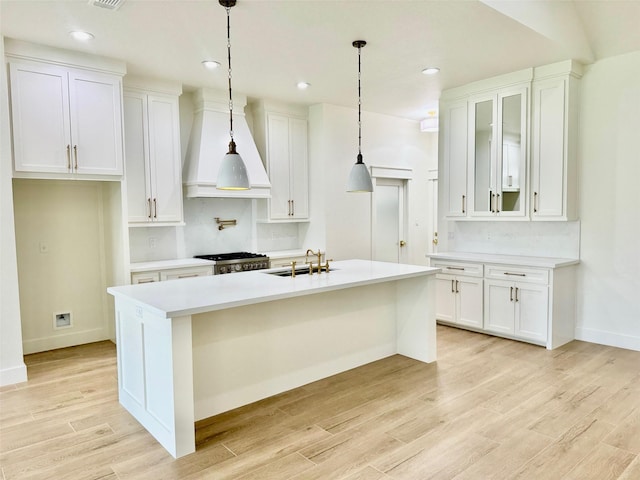 kitchen featuring white cabinetry, a center island with sink, stove, and premium range hood