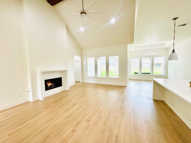 unfurnished living room featuring beamed ceiling, high vaulted ceiling, ceiling fan with notable chandelier, and light hardwood / wood-style floors