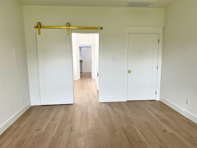 unfurnished bedroom with a barn door and light hardwood / wood-style flooring