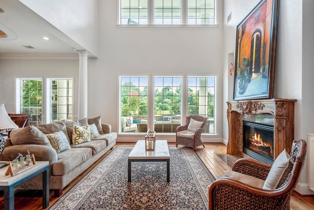 living room featuring ornamental molding, wood-type flooring, a premium fireplace, decorative columns, and a high ceiling