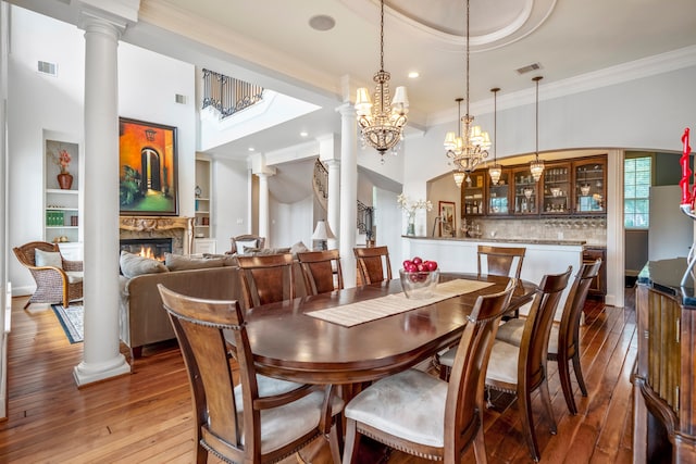 dining area with wood-type flooring, an inviting chandelier, a high end fireplace, and ornate columns