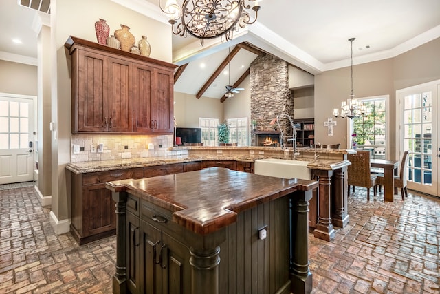 kitchen with high vaulted ceiling, a stone fireplace, a kitchen island, butcher block counters, and decorative light fixtures