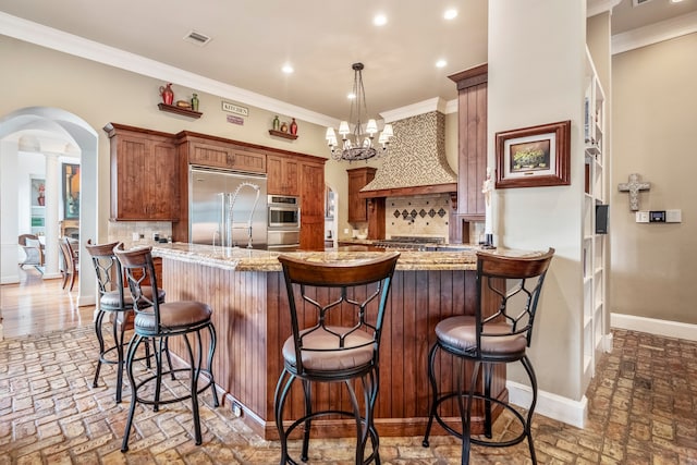 kitchen with a kitchen bar, an inviting chandelier, backsplash, appliances with stainless steel finishes, and light stone countertops