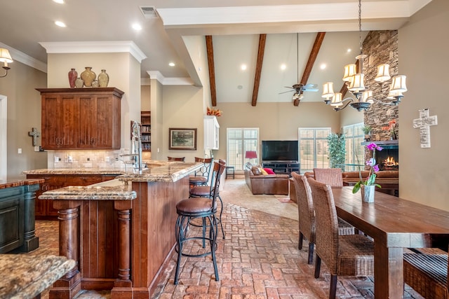 kitchen with backsplash, a fireplace, light stone countertops, pendant lighting, and ornamental molding