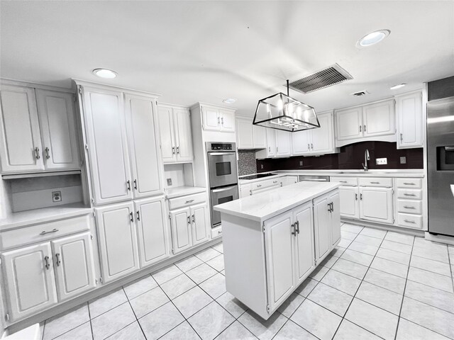 kitchen with appliances with stainless steel finishes, white cabinetry, light tile patterned flooring, and a kitchen island