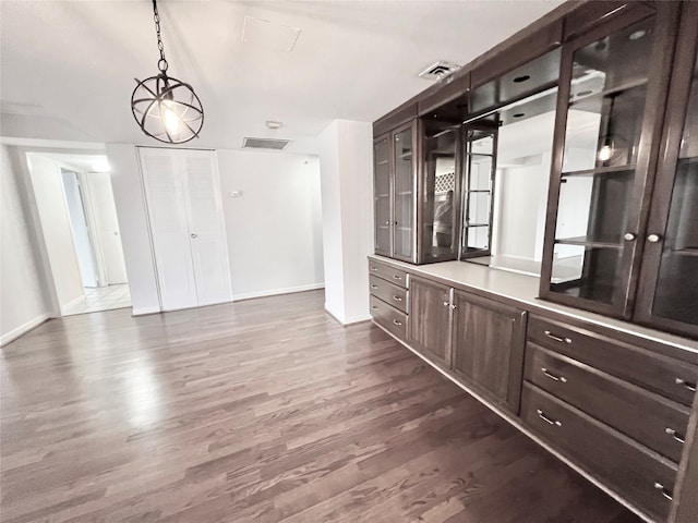 bar with dark wood-type flooring, dark brown cabinets, pendant lighting, and an inviting chandelier