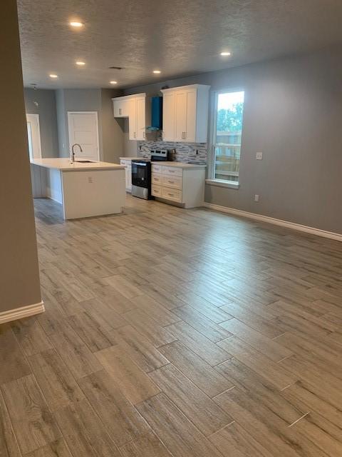 kitchen featuring sink, white cabinets, a kitchen island with sink, light wood-type flooring, and electric stove