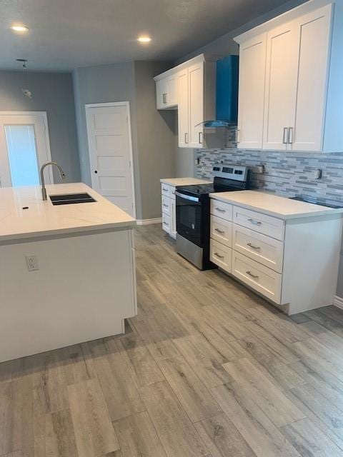 kitchen featuring stainless steel electric range, sink, light hardwood / wood-style flooring, white cabinets, and wall chimney exhaust hood