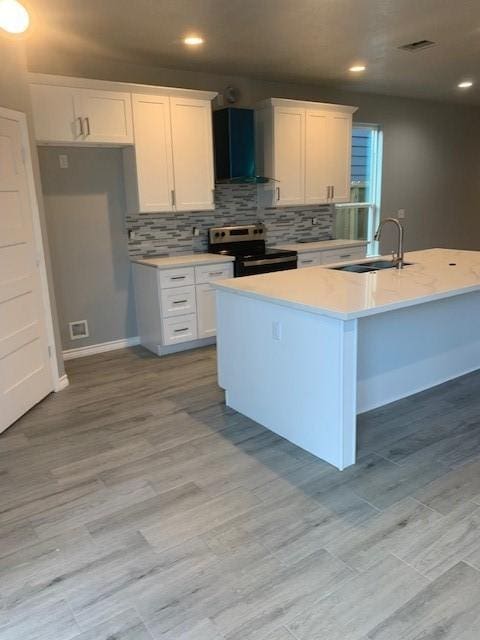 kitchen featuring electric stove, wall chimney range hood, sink, and white cabinets