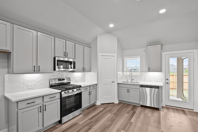 kitchen featuring appliances with stainless steel finishes, vaulted ceiling, light countertops, light wood-type flooring, and a sink