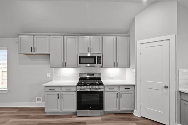 kitchen with lofted ceiling, stainless steel appliances, decorative backsplash, and light countertops