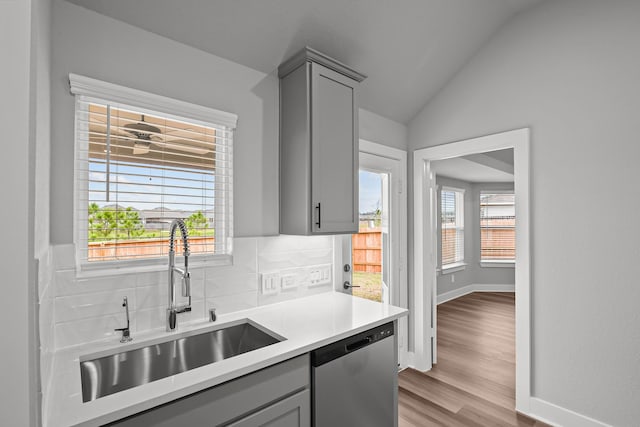 kitchen featuring dishwasher, backsplash, a sink, and gray cabinetry