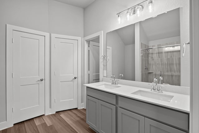 full bath with a tile shower, double vanity, wood finished floors, and a sink