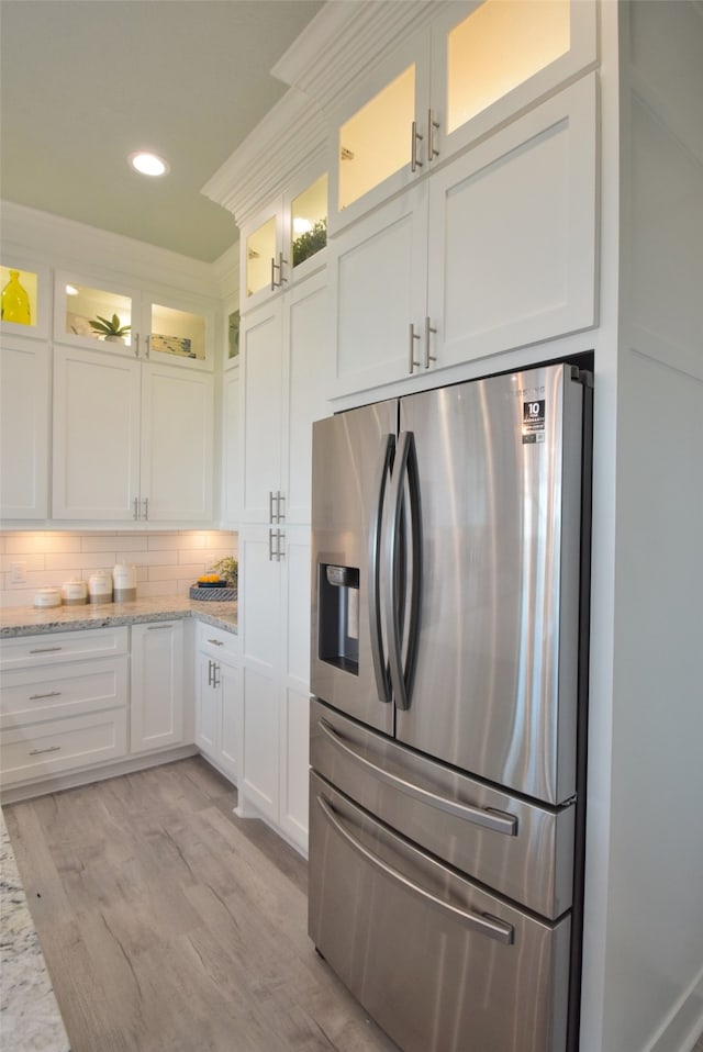 kitchen with light hardwood / wood-style flooring, stainless steel refrigerator with ice dispenser, decorative backsplash, and light stone countertops