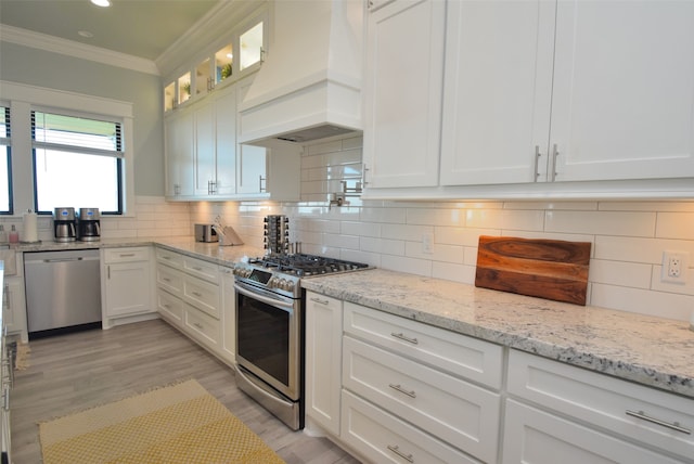 kitchen featuring white cabinetry, custom range hood, backsplash, stainless steel appliances, and light hardwood / wood-style floors