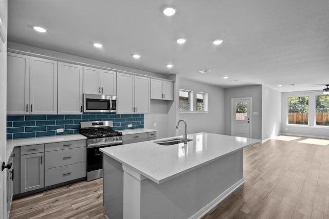 kitchen featuring a center island with sink, stainless steel appliances, light wood-type flooring, and sink