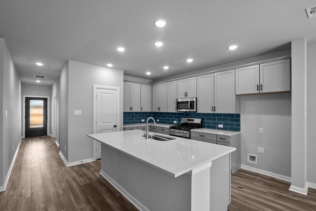 kitchen with a center island with sink, sink, dark hardwood / wood-style floors, light stone countertops, and stainless steel appliances