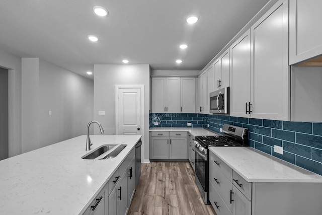 kitchen featuring sink, light stone counters, light hardwood / wood-style flooring, backsplash, and appliances with stainless steel finishes