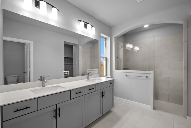 bathroom featuring tile patterned flooring, a tile shower, vanity, and toilet