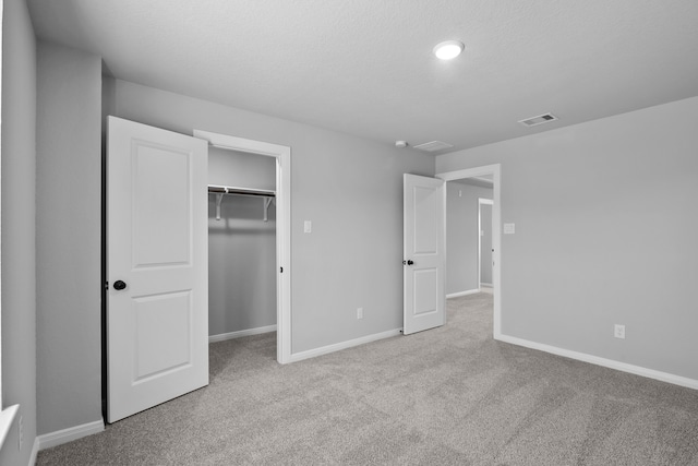 unfurnished bedroom with a textured ceiling, light colored carpet, and a closet