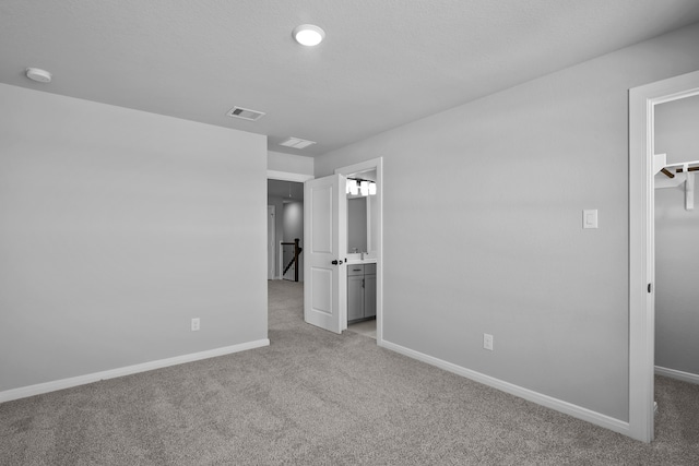 unfurnished bedroom featuring light carpet, a closet, a spacious closet, and ensuite bath