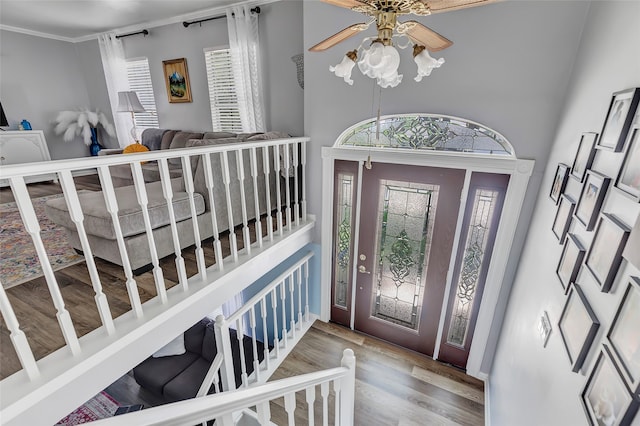 entryway featuring ceiling fan, wood-type flooring, ornamental molding, and a towering ceiling