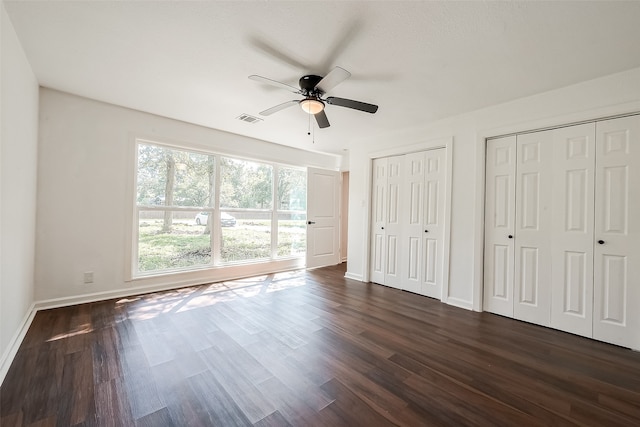 unfurnished bedroom featuring two closets, dark wood-type flooring, and ceiling fan