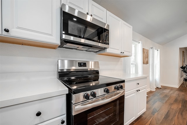 kitchen with lofted ceiling, stainless steel appliances, white cabinets, and dark hardwood / wood-style flooring