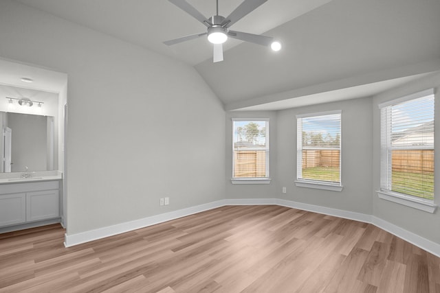 unfurnished bedroom with lofted ceiling, connected bathroom, a sink, baseboards, and light wood-style floors