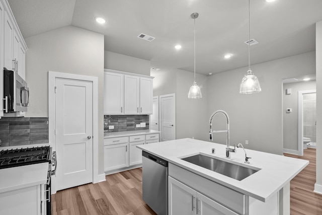 kitchen featuring stainless steel appliances, a sink, visible vents, white cabinetry, and a center island with sink