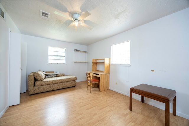 living area featuring light wood-type flooring, ceiling fan, and a textured ceiling