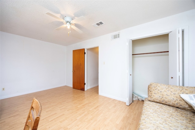 bedroom with light hardwood / wood-style floors, a closet, a textured ceiling, and ceiling fan