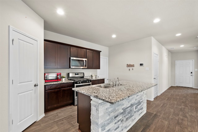 kitchen featuring hardwood / wood-style flooring, stainless steel appliances, an island with sink, sink, and light stone counters