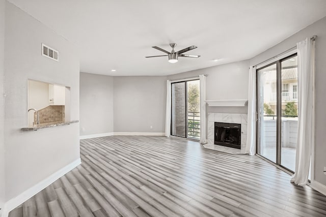 unfurnished living room featuring a tiled fireplace, light wood-type flooring, and ceiling fan