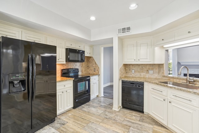 kitchen featuring tasteful backsplash, light stone countertops, black appliances, sink, and white cabinetry