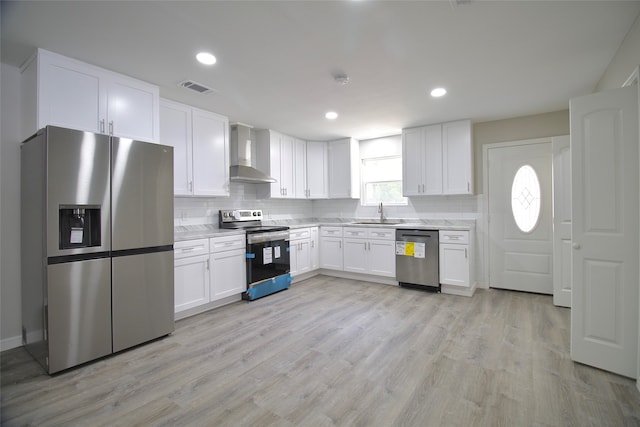 kitchen with white cabinets, light hardwood / wood-style flooring, appliances with stainless steel finishes, and wall chimney range hood