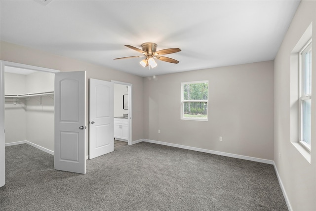 unfurnished bedroom with a walk in closet, ceiling fan, baseboards, and dark colored carpet