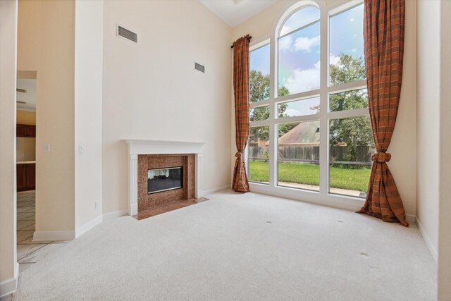 unfurnished living room with a tiled fireplace, light carpet, and a towering ceiling